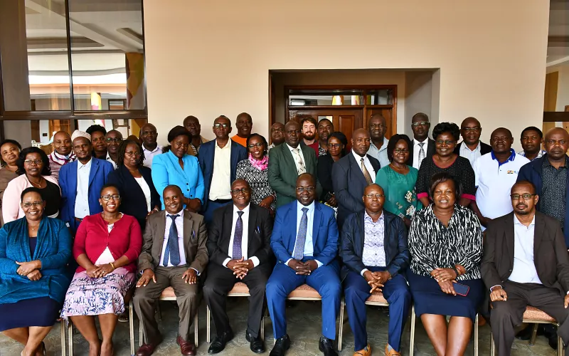 A diverse group of 34 people, mixed genders, in business attire, pose indoors for a group photo.