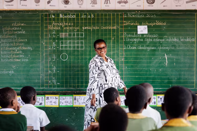 A female teacher in South Africa standing in front of a blackboard teaching her students.