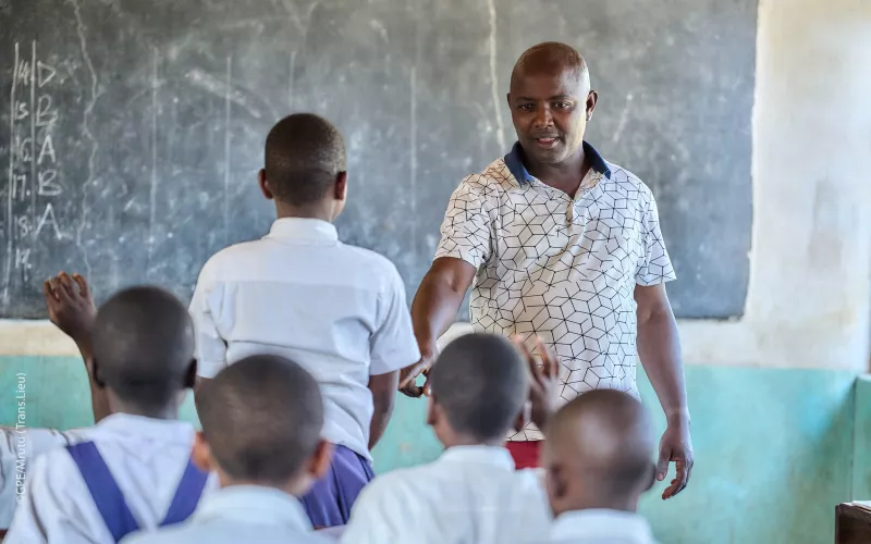 Male teacher interacting with students in a classroom in Tanzania.