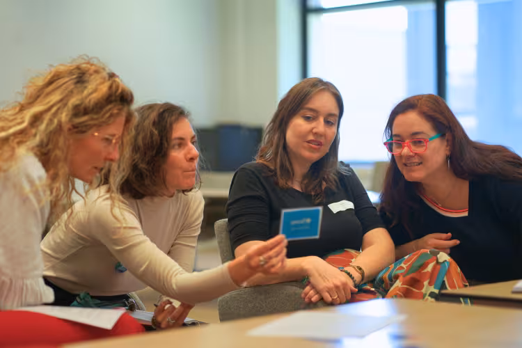 Four women looking at a blue card and discussing.