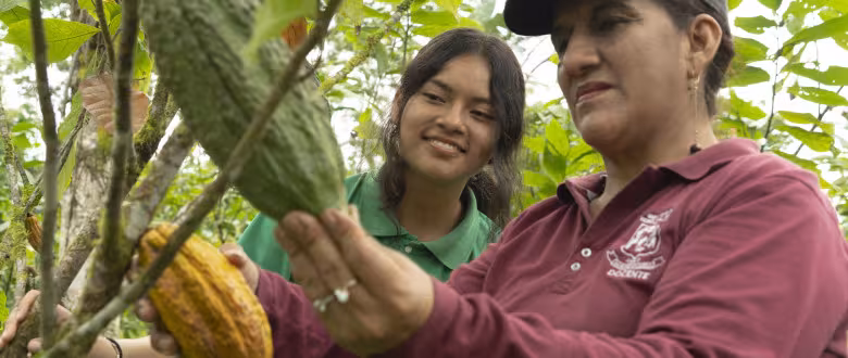 Woman showing a young lady a cocoa pod.