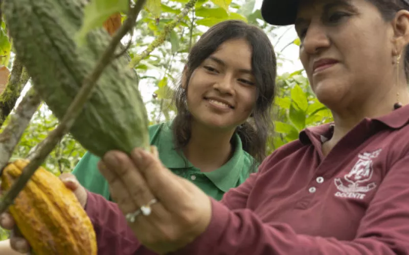 Woman showing a young lady a cocoa pod.