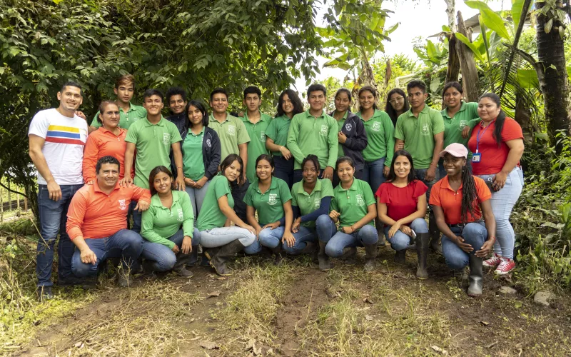 A group of young people and adults pose outdoors against lush greenery.