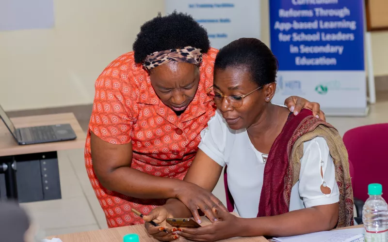 Two women focus on a smartphone, with one assisting the other.
