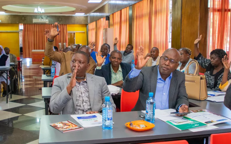Several people sitting at desks and raising their hands.