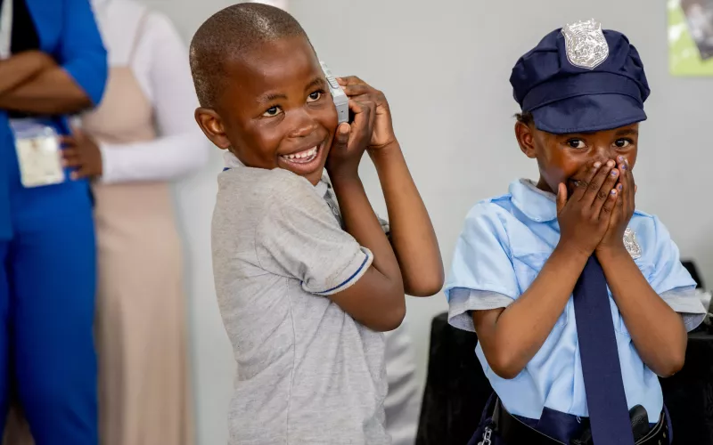 Smiling children role play different jobs such as police officer in South Africa, showing gender shouldn't matter in jobs.