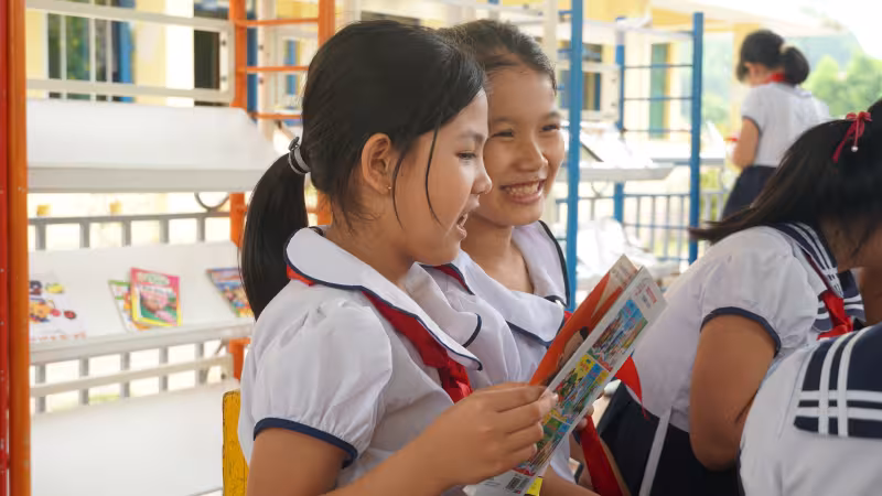 Two female Vietnamese students in enjoy reading a book together