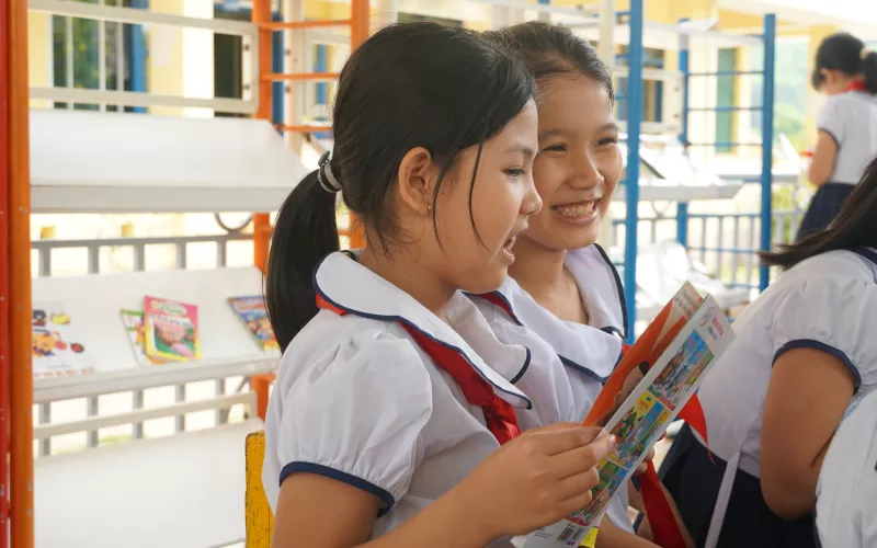 Two female Vietnamese students in enjoy reading a book together