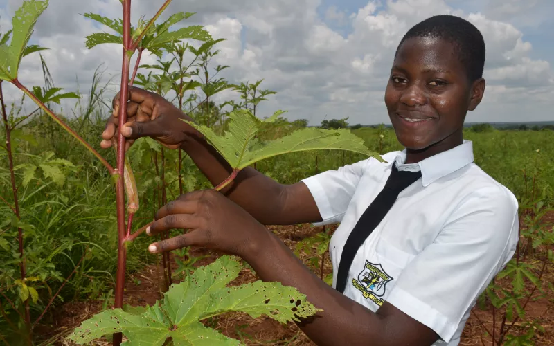 An agricultural student in Uganda poses with a plant