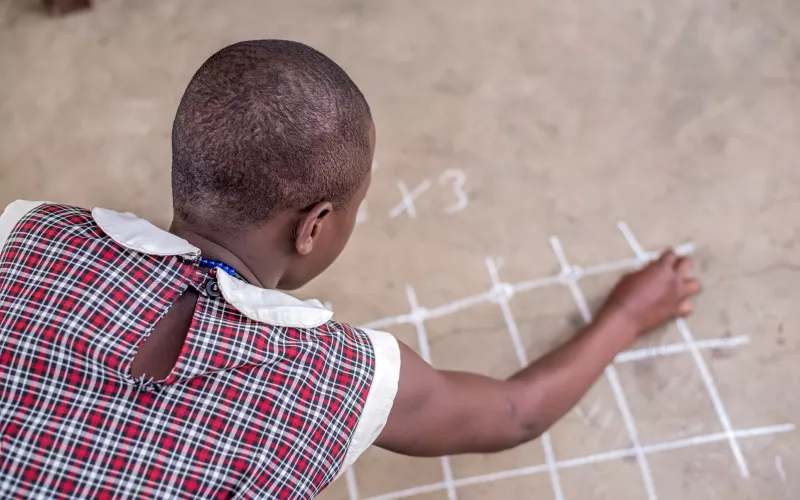 A schoolgirl does maths using chalk on the ground