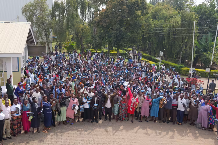 A large group of people stand outdoors raising their hands in celebration