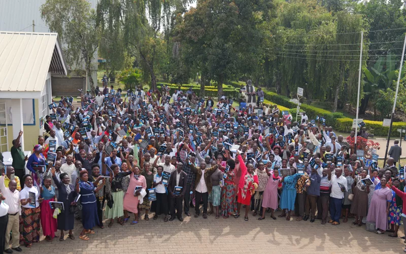 A large group of people stand outdoors raising their hands in celebration