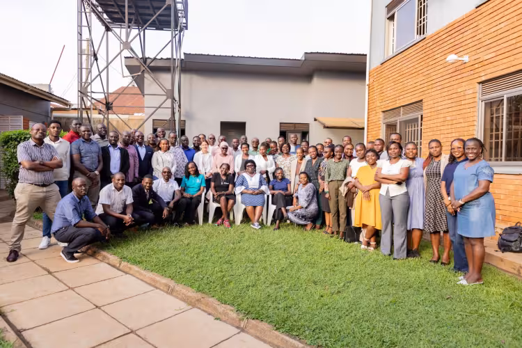 A large group of people is gathered outdoors in front of two adjacent buildings, standing and sitting together for a group photo.