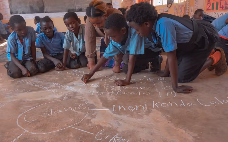 Learners in Zambia draw on the classroom floor with their teacher as part of the Catch Up programme