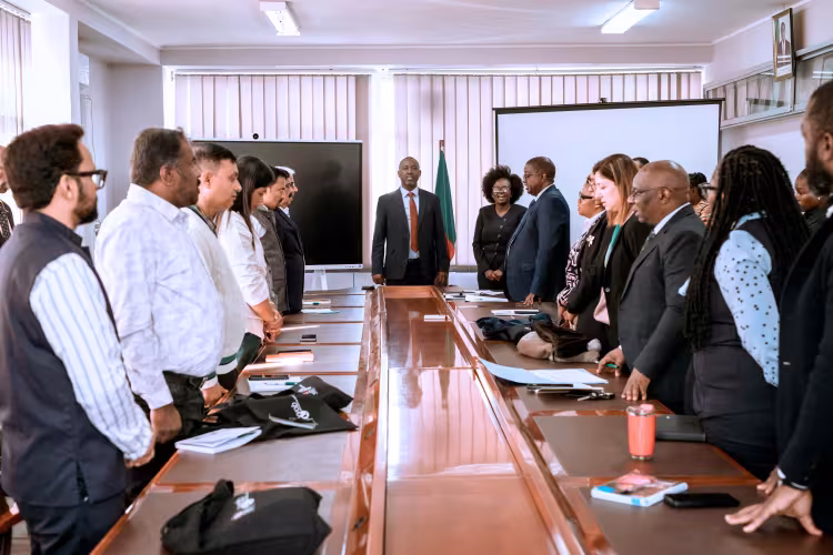 Education leaders from Zambia and India standing around a rectangular conference table during a meeting in a boardroom.