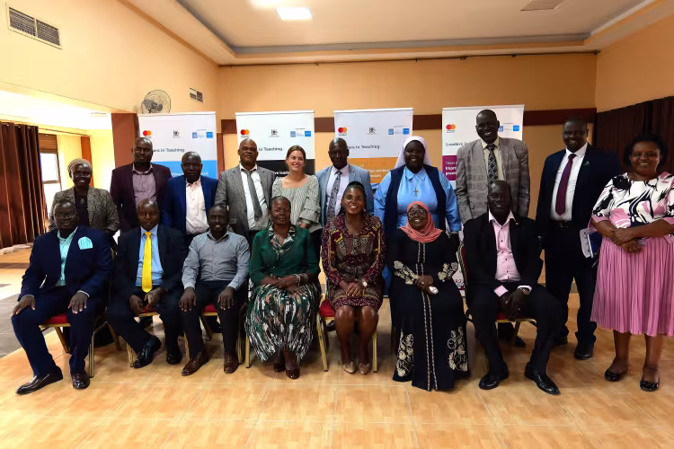 A group people in a conference room seated and standing rows. Behind them are Leaders in Teaching programme branded banners