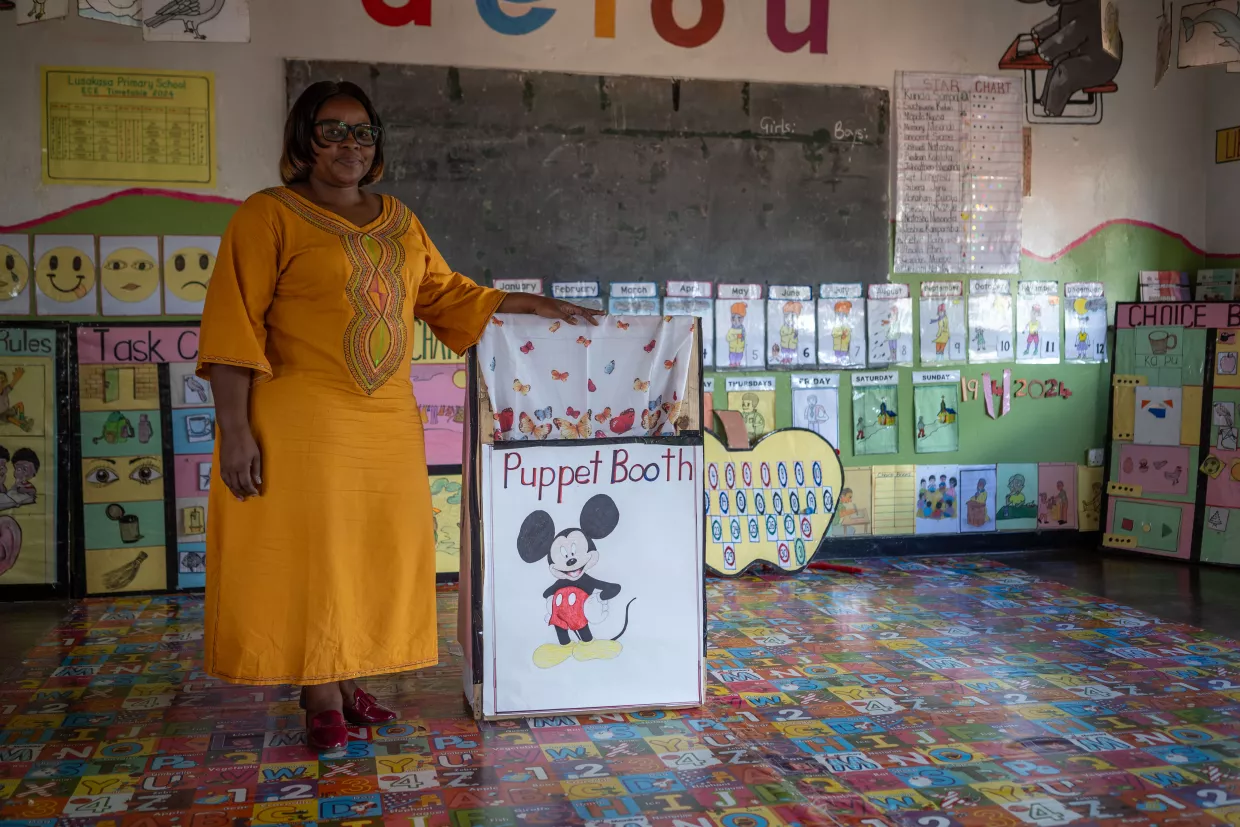 Early childhood education teacher Ngandu Siamwaanja posing with her self-made puppet theatre in her classroom.
