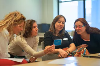 Four women looking at a blue card and discussing.