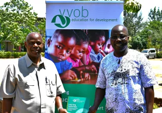 Two men stand smiling in front of a VVOB  banner.