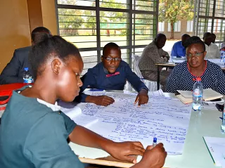 A group of people engaged in a collaborative discussion at a table, writing on a large paper.