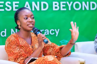 A women speaking to the audience holding a microphone.