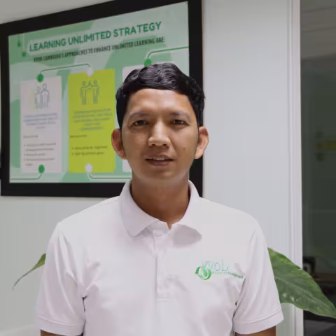 Phealay wearing a white VVOB polo shirt, standing in front of a frame VVOB banner that reads 'Learning Unlimited Strategy.'