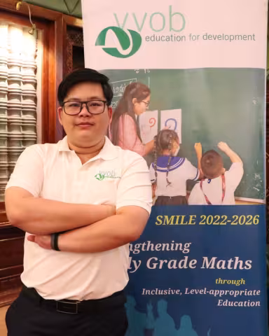 Sotheavny wearing a white VVOB polo shirt, standing in front of a VVOB banner.