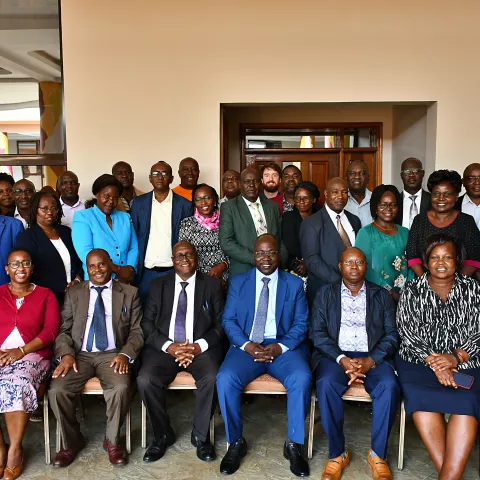 A diverse group of 34 people, mixed genders, in business attire, pose indoors for a group photo.