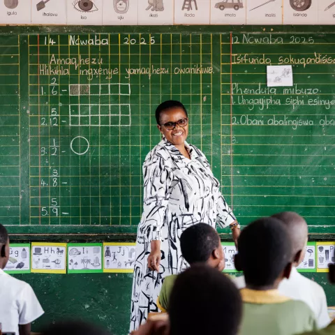 A female teacher in South Africa standing in front of a blackboard teaching her students.