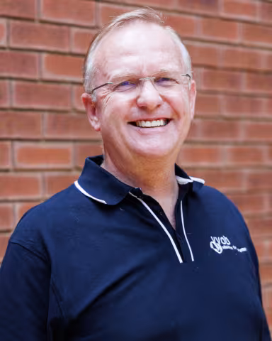 Gerrit smiling in a navy polo shirt stands against a brick wall. His expression is warm and friendly.