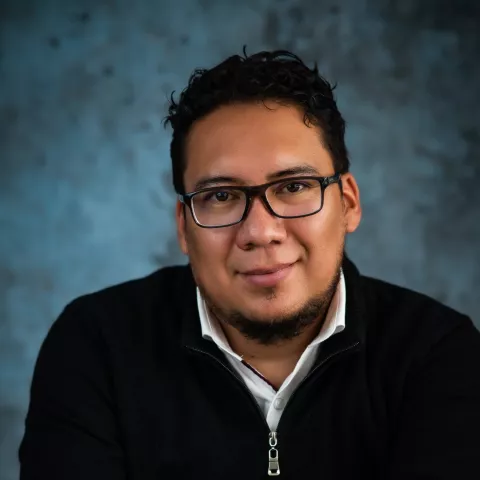 Luis smiles softly at the camera while wearing a black crew neck sweater. 
