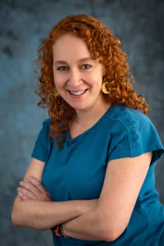 Maria smiles at the camera with her arms crossed, wearing a blue shirt.
