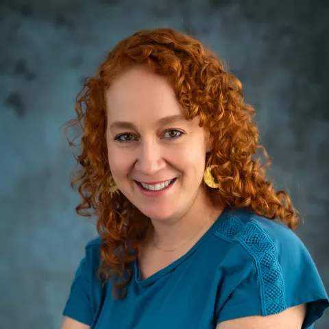 Maria smiles at the camera with her arms crossed, wearing a blue shirt.