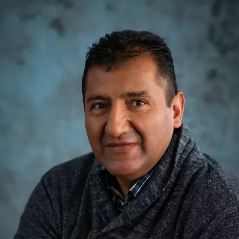 Milton smiles softly looking into the camera. He is wearing a dark grey sweater.