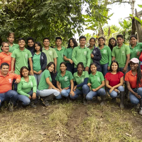 A group of young people and adults pose outdoors against lush greenery.