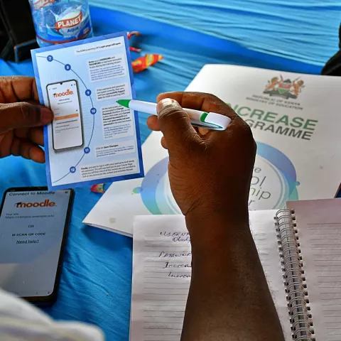 A person holds a brochure with a pen on a blue surface.