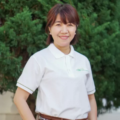 Phuc smiles warmly, wearing a white VVOB polo shirt. She stands against a backdrop of lush green foliage.