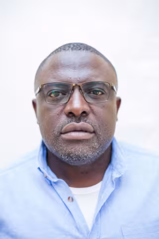 Aaron is wearing a blue shirt and glasses. The background is plain white.