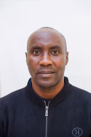 Andrew has a neutral expression and looks directly at the camera. He's wearing a black zip-up jacket with a subtle logo. The background is plain white.