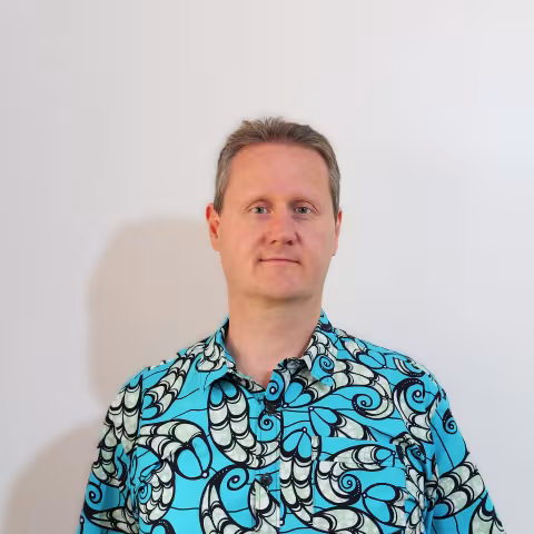 Bram wearing a bright blue, patterned shirt stands against a plain white background. He has short hair and a neutral expression.