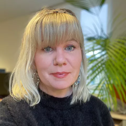 Christine is wearing a black turtleneck and smiles into the camera. The background is blurred plants.