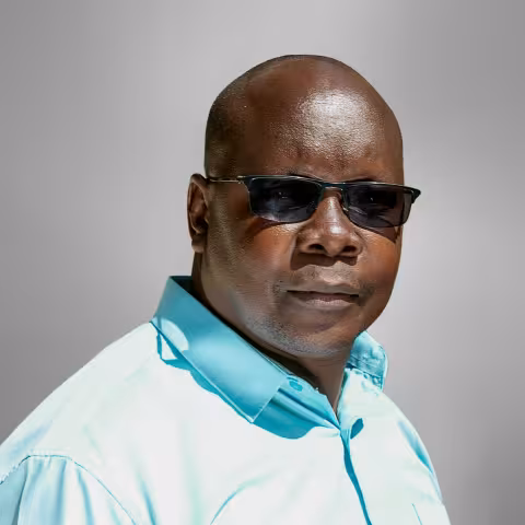 Collins is in sunglasses and wearing a light blue shirt. He stands against a neutral gray background.