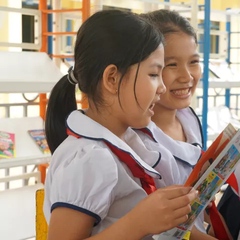 Two female Vietnamese students in enjoy reading a book together