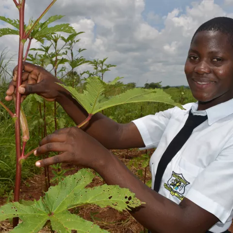 An agricultural student in Uganda poses with a plant