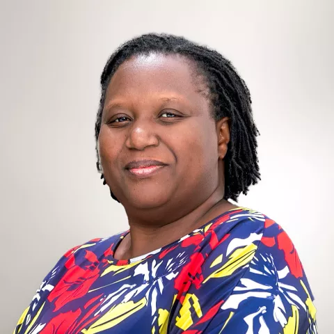 Doris smiles. She is wearing a colourful top. The background is light gray. 