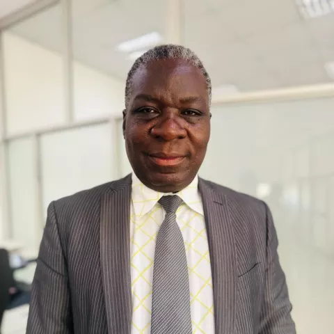 Fabian is wearing a suit with a patterned tie, standing in a bright office. 