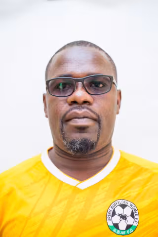 Felix is wearing glasses and a yellow "Green Buffaloes Women FC" jersey. He stands against a white background, conveying a serious, focused expression.