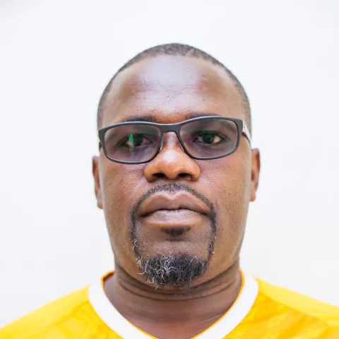 Felix is wearing glasses and a yellow "Green Buffaloes Women FC" jersey. He stands against a white background, conveying a serious, focused expression.