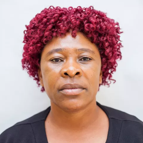 Gift has red curly hair. She is wearing a black cardigan over a red top. The background is plain white. 