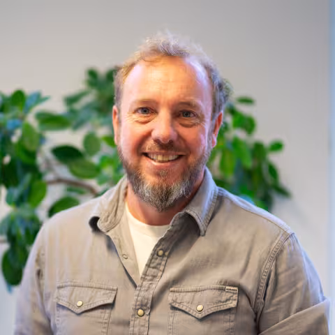 Hans is smiling the camera, wearing a light-brown shirt.
